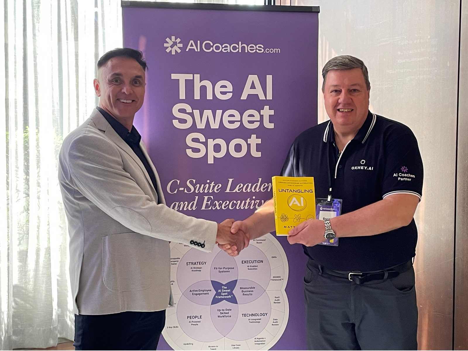 Two attendees shaking hands with a copy of Untangling AI in front of The AI Sweet Spot banner at the Sydney breakfast session.